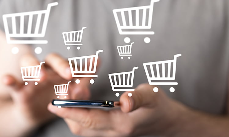 A photo of a woman holding a cell phone with cartoon shopping carts surrounding her hands.